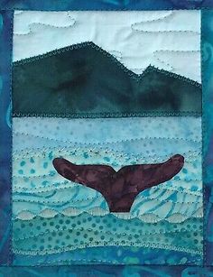 a blue quilted wall hanging with a whale tail in the water and mountains behind it