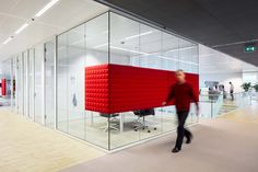 a person walking in an office area with glass walls and red furniture on the floor