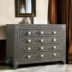 an ornate black and white chest of drawers in a living room with a mirror on the wall