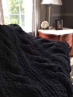 a bed with a black blanket on top of it next to a dresser and lamp