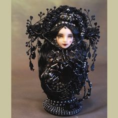 a doll is sitting in a black vase with beads on it's head and arms