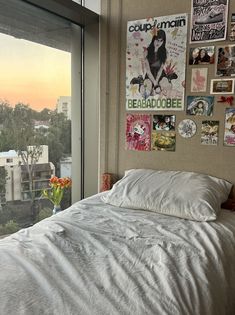 a bed sitting in front of a window next to a wall with pictures on it