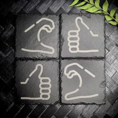 four square slate coasters with hand symbols and green leaves on the top one has two fingers pointing at each other