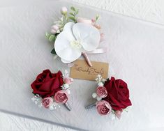 two boutonnieres with red and white flowers on top of a bed sheet