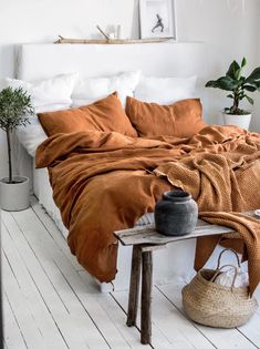 a bed with an orange blanket on top of it next to a table and potted plant