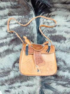 This genuine leather saddle purse is an absolute must-have! It's modeled after a saddle for a truly unique design. Plus, it features an adjustable shoulder strap so you can adjust the fit. An out-of-the-box way to accessorize with flair! Tooled Leather Saddle Purse: Measures appx. 10" x 9" x 4". Crafted of genuine leather. Available in tan & brown. Comes with adjustable strap. Made in Mexico. Weight: 2 lbs. Visit us on Facebook for inspirational ideas on decorating any space. Don't forget to fol Saddle Bag With Detachable Strap For Daily Use, Daily Use Saddle Shoulder Bag With Adjustable Strap, Daily Use Shoulder Bag With Adjustable Strap Saddle Shape, Daily Use Saddle Bag With Adjustable Strap, Saddle Bag With Removable Pouch For Daily Use, Travel Saddle Bag With Adjustable Strap, Daily Use Saddle Bag With Removable Pouch, Western Leather Shoulder Bag For Everyday Use, Western Saddle Bag For Everyday Use