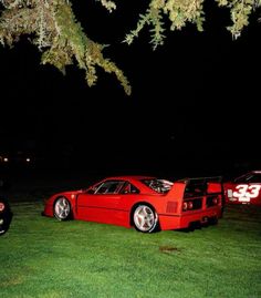 a red sports car parked in the grass under a tree at night with lights on