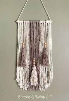 a macrame wall hanging with tassels and buttons on the bottom, attached to a gray wall