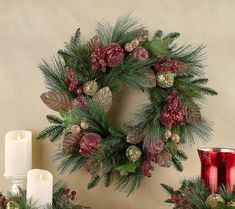 a christmas wreath with pine cones, berries and greenery is displayed next to candles