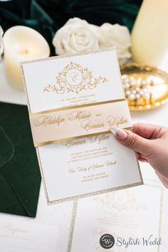 a person holding up a wedding card in front of a table with candles and flowers