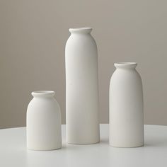 three white vases sitting on top of a table