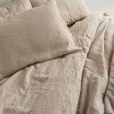 an unmade bed with two pillows on top of it and a white wall in the background