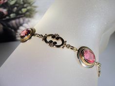 "This is a beautiful rose pink bracelet that is 14k Gold Filled. There are 4 oval cut faceted rosy pink glass gems with a decorative scroll link in between each. The look is stunning! Size of the bracelet is 7.25 inches. It has a round twist closure and a safety chain that is also able to be released and attached with the same type of closure. *Hang Tag reads: AMCO, 1/20 14K Gold Filled *Length is 7.25 inches *Width is .5 inches *Condition is Excellent = in \"LIKE NEW\" Condition; Pre-owned To v Elegant Rose Gold Bracelet For Formal Occasions, Elegant Pink Gold Bracelet For Formal Occasions, Elegant Pink Gold Round Bracelet, Adjustable Pink Gold Bracelet For Formal Occasions, Adjustable Pink Gold Bracelets For Formal Occasions, Pink Round Antique Jewelry, Antique Pink Round Jewelry, Formal Pink Gold Bracelet, Classic Pink Jewelry With Bezel Setting