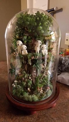 a glass dome filled with plants and small stuffed animals on top of a wooden base