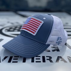 Slate & White Mesh-Back Trucker Hat Custom Made Right Here In The USA! 🇺🇸 This slate fabric and white mesh trucker hat has an oversized full-color American flag and branded side panel. ✅ Our classic trucker hats are structured with a higher profile ✅ Pre-curved visor ✅ Snap-back closure ✅ Branded side panel ✅ Moisture-wicking sweatband ✅ Classic top button ✅ Superior quality, comfort, and American craftsmanship. Trucker Style Baseball Cap With Flat Bill, Trucker Baseball Cap With Flat Brim For Baseball Season, White Adjustable Trucker Dad Hat, Summer Trucker Snapback Hat With Six-panel Design, Summer Trucker Snapback Hat Six-panel, Trucker Style Baseball Cap For Baseball Season, Trucker Hat With Flat Brim For Sports, Patriotic Baseball Cap For Outdoor, White Cap For Memorial Day