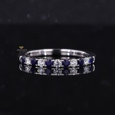 a white gold ring with blue sapphires and diamonds on the side, in front of a black background