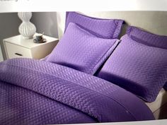 a bed with purple sheets and pillows on it