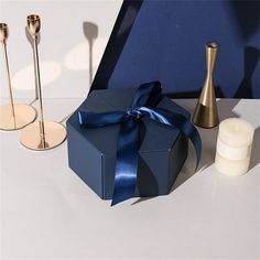 two candles and a gift box with a blue ribbon on a white table next to it