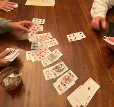 several people playing cards on a wooden table