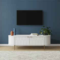 a tv is mounted on the wall above a white cabinet with two vases and a potted plant