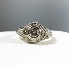 This is a gorgeous platinum antique ring that features a beautiful central diamond. The design of this ring is outstanding. It has very detailed filigree and carving and engraving goes halfway down the band. The diamond is a bezel set brilliant cut diamond and weighs .57 carats. It is a very clean VS-1 and G color. It has a ton of sparkle! There are 2 more diamonds on the shoulders and 2 on the gallery side. The total weight is estimated at .70 carats. All the diamonds are clean and sparkly. It Heirloom Silver Engraved Ring With Center Stone, Antique White Wedding Dress With Intricate Design, Antique Engraved Diamond Ring With Accents, Vintage Formal Filigree Ring With Single Cut Diamonds, Ornate Filigree Diamond Ring With Brilliant Cut, Ornate Brilliant Cut Ring For Anniversary, Vintage Filigree Ring With Diamond Cut, Antique Silver Engraved Ring With Diamond Cut, Ornate Round Diamond Ring With Center Stone