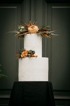 a three tiered white wedding cake with orange flowers on top and greenery around it