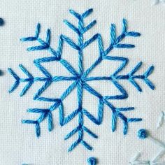 a blue snowflake is stitched onto a white piece of fabric with thread