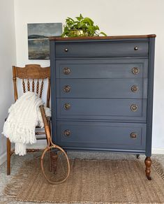 a blue dresser with a tennis racket on top and a plant in the corner