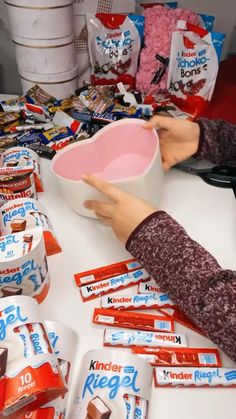 a person holding a bowl over a table full of candy bar wrappers and candies