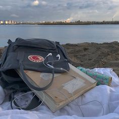 an open book and headphones are sitting on a blanket by the water