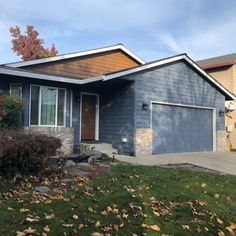 a blue house in the fall with leaves on the grass and trees around it,