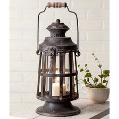 an old fashioned lantern with two lit candles on the table next to a potted plant