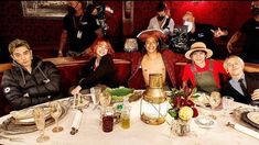 a group of people sitting around a table with plates and glasses on it, posing for the camera