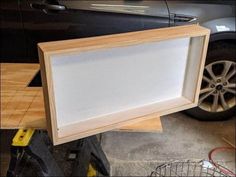 a wooden frame sitting on top of a table next to a car