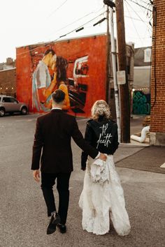 a bride and groom walking down the street holding hands in front of a graffiti wall