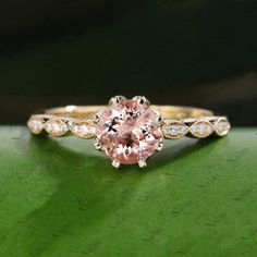 an engagement ring with a pink diamond in the center on top of a green surface