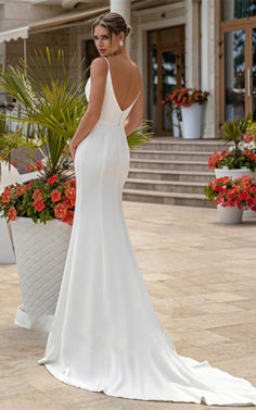 a woman in a white wedding dress standing on the ground near some potted plants