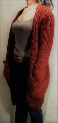 a woman standing in front of a white wall wearing a red cardigan sweater and jeans