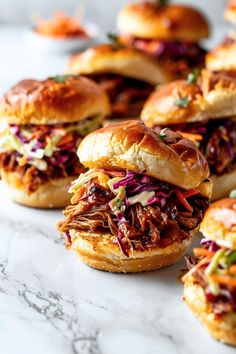 several pulled pork sliders with coleslaw slaw on the side, lined up on a marble countertop