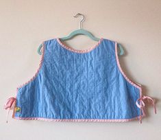 a child's blue and pink top hanging on a wall with a wooden hanger