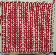 a piece of red and white weaving on a wooden board