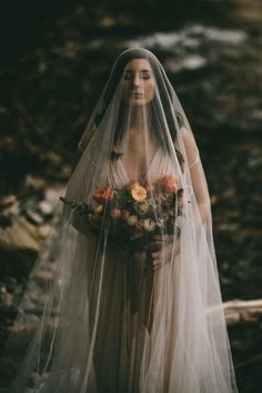 a woman wearing a veil and holding a bouquet in her hands is standing near a stream