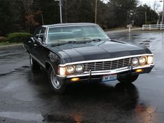 an old black car is parked in the parking lot on a rainy day with no one around