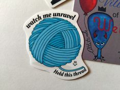 two magnets with words on them and an image of a blue ball of yarn