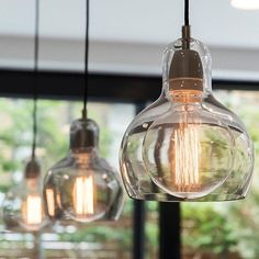 three light bulbs hanging from a ceiling in front of a window with trees and bushes