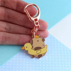 a hand holding a gold colored key chain with a cartoon character charm attached to it