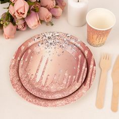 pink plates and utensils on a white table with flowers, candles and napkins