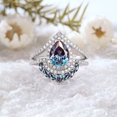 a blue and white diamond ring sitting on top of a snow covered ground with flowers in the background