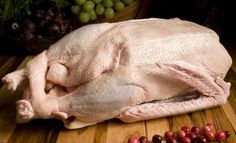 a whole chicken sitting on top of a wooden table next to grapes and other fruits