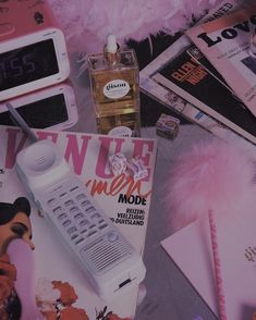 an assortment of electronic devices and magazines on a table with pink feathers in the background